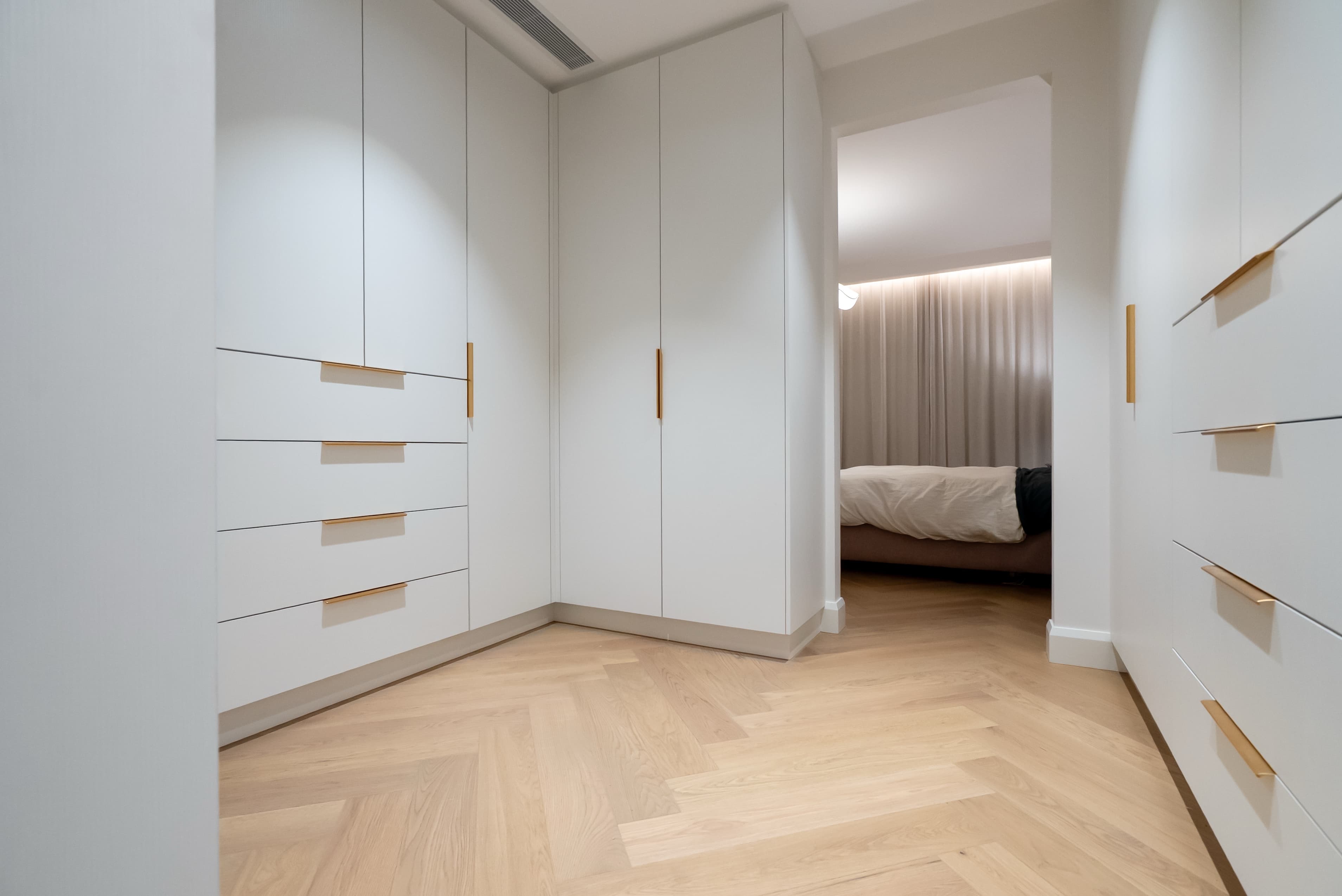 Walk-in wardrobe with white cabinetry and gold handles