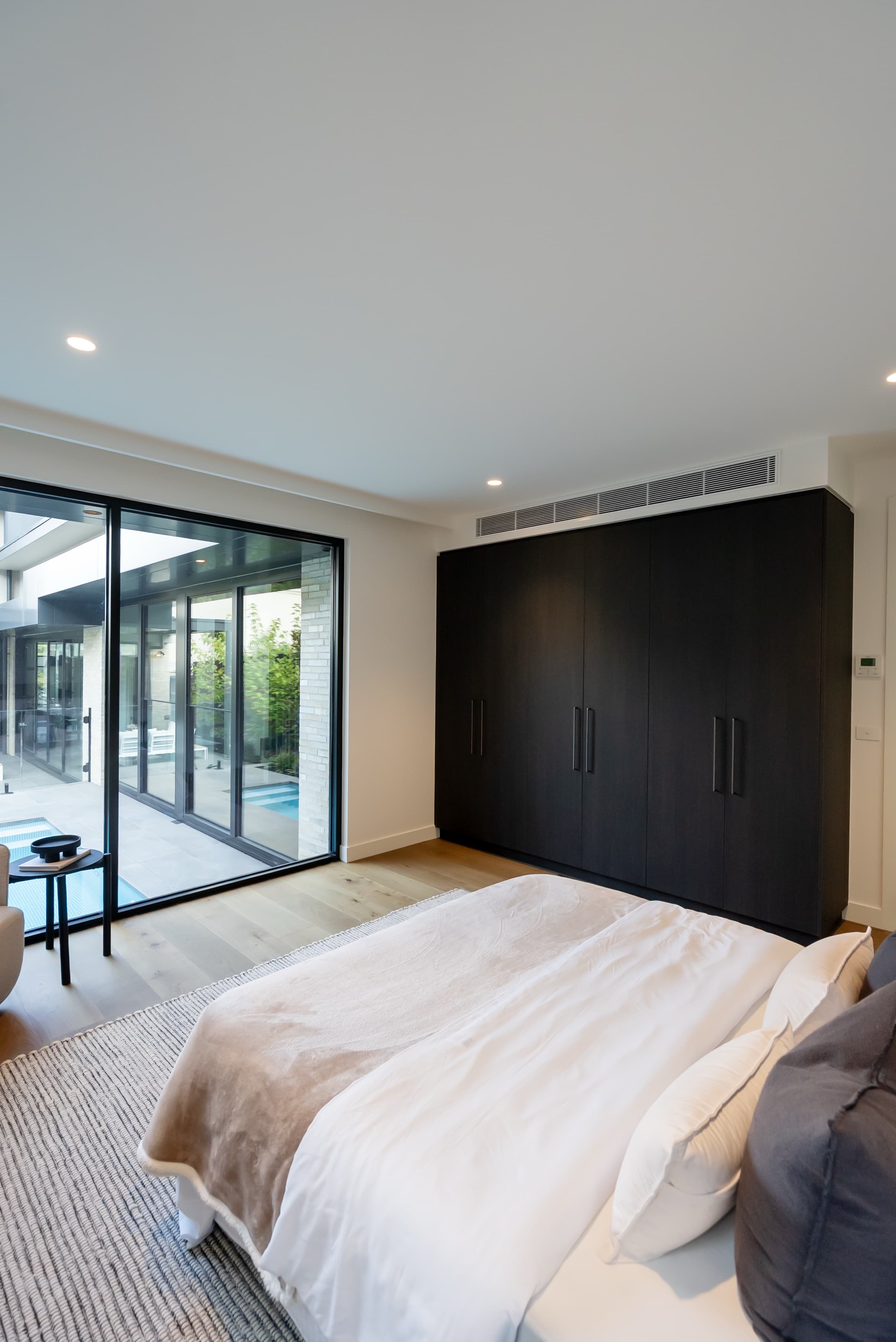 Modern bedroom with dark built-in wardrobes and pool view